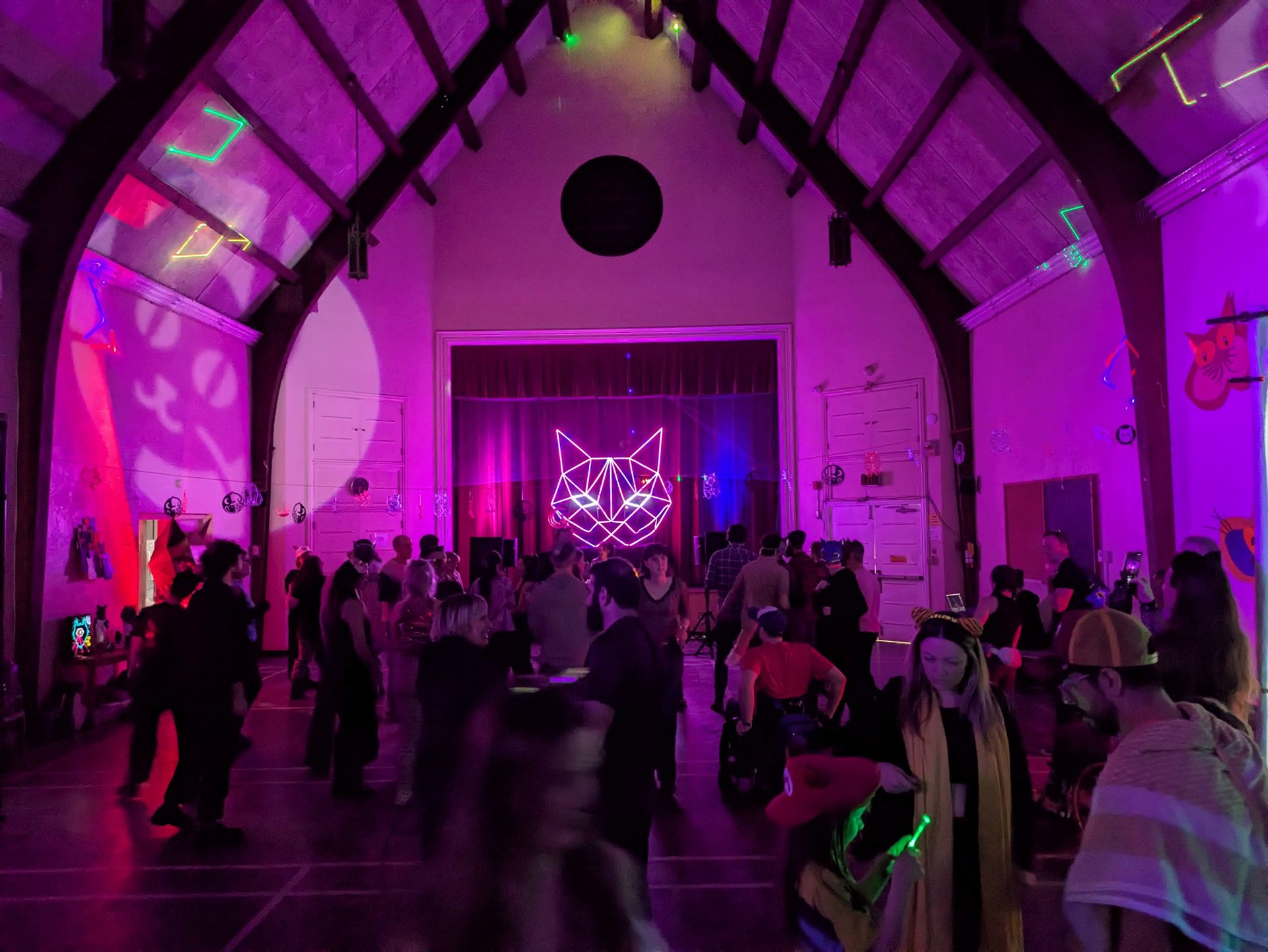 The lit sculpture on the stage at the far end of a packed hall, the whole room washed in magenta.