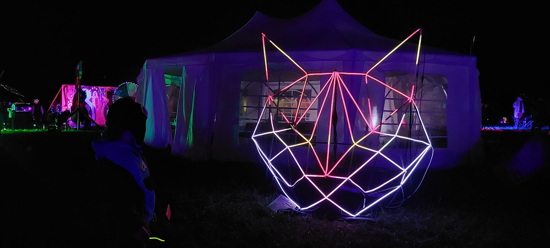 The sculpture glowing pink and white against a marquee at night, a visitor watching from the dark.