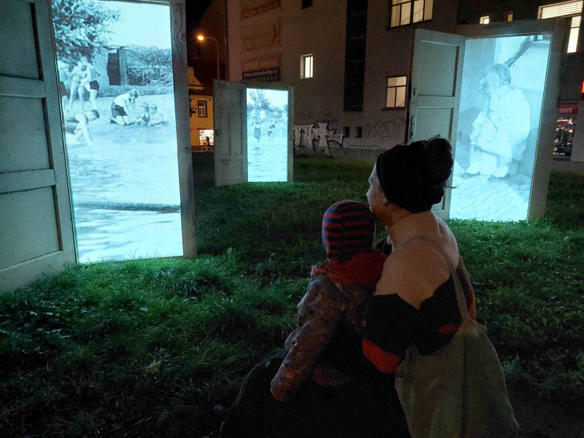 A woman holding a small child, both watching the projections between the open doors.