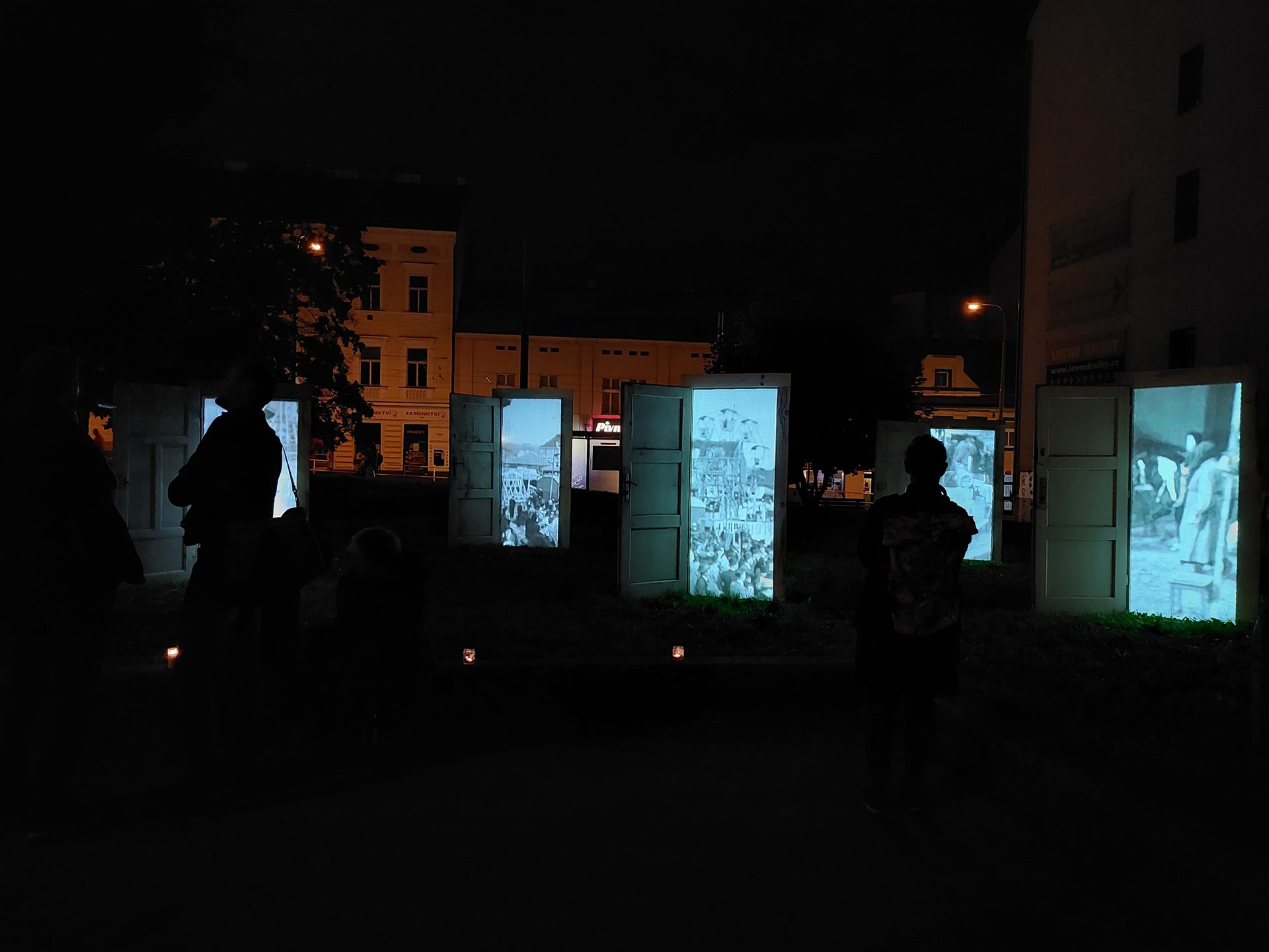 The row of doors seen across the park, visitors passing in silhouette.