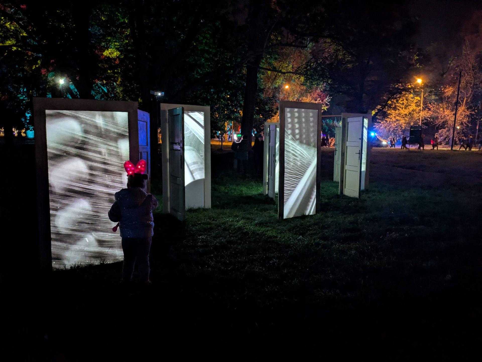 A child looking up at one of the doors, the rest of the row receding into the dark park.